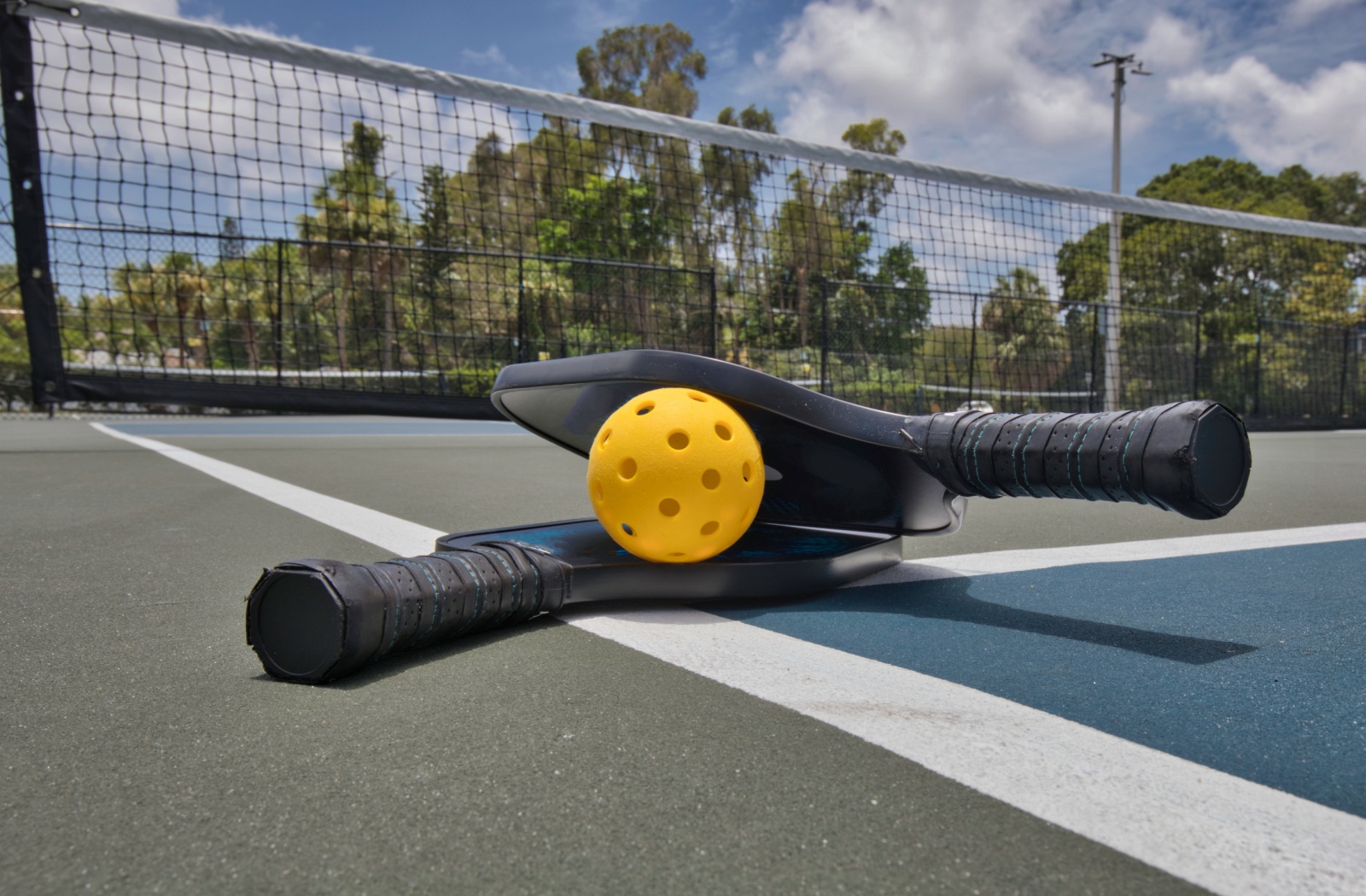 Two pickleball paddles with a ball sit on an outdoor court.