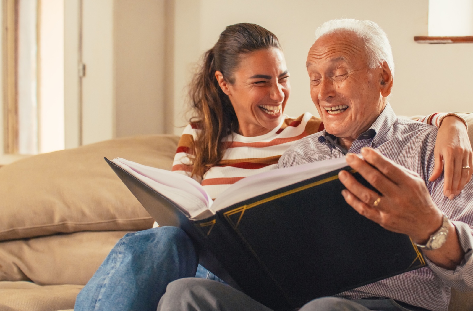 A smiling senior in assisted living reads a memory book with their child during a visit.