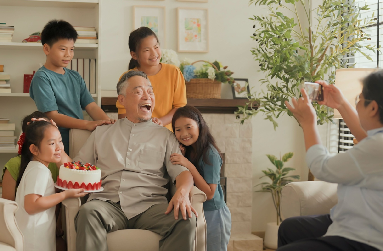 A group of grandchildren crowd around their grandparents with a birthday cake while visiting.