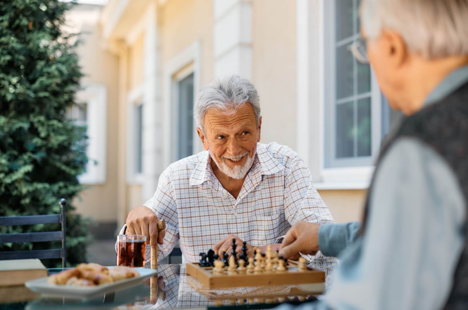 Two older adults playing chess outside on a patio in an independent living community.
