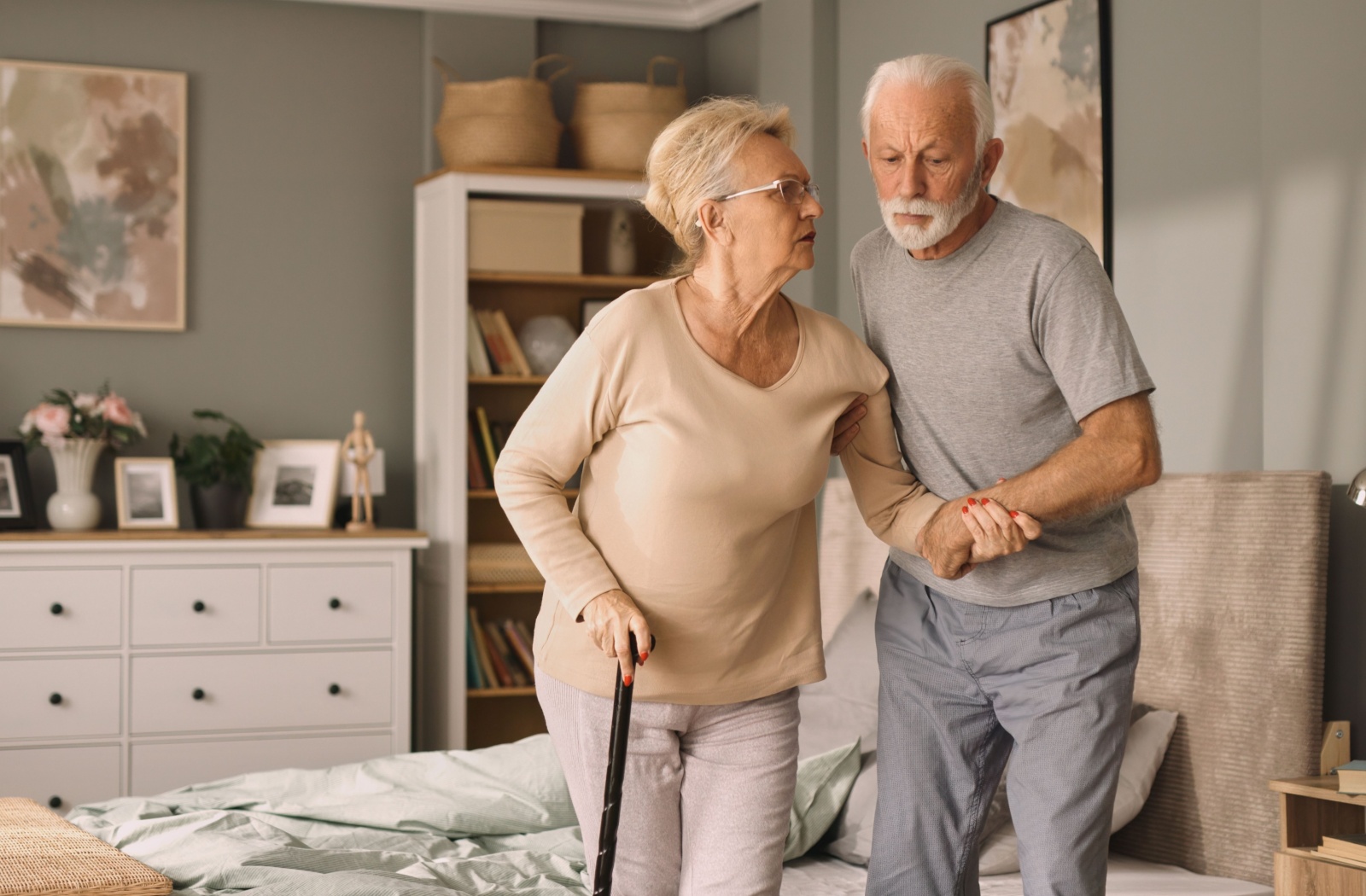 An older adult helping their spouse move around their home.