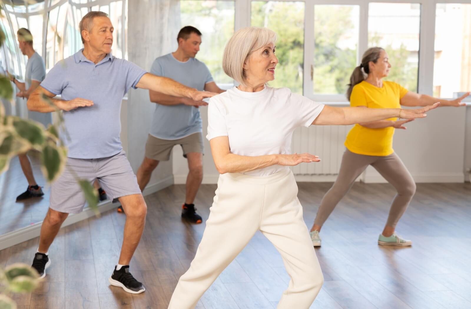 A group of older adults practicing tai chi in a bright indoor studio, focusing on balance, coordination, and gentle movement for wellness.