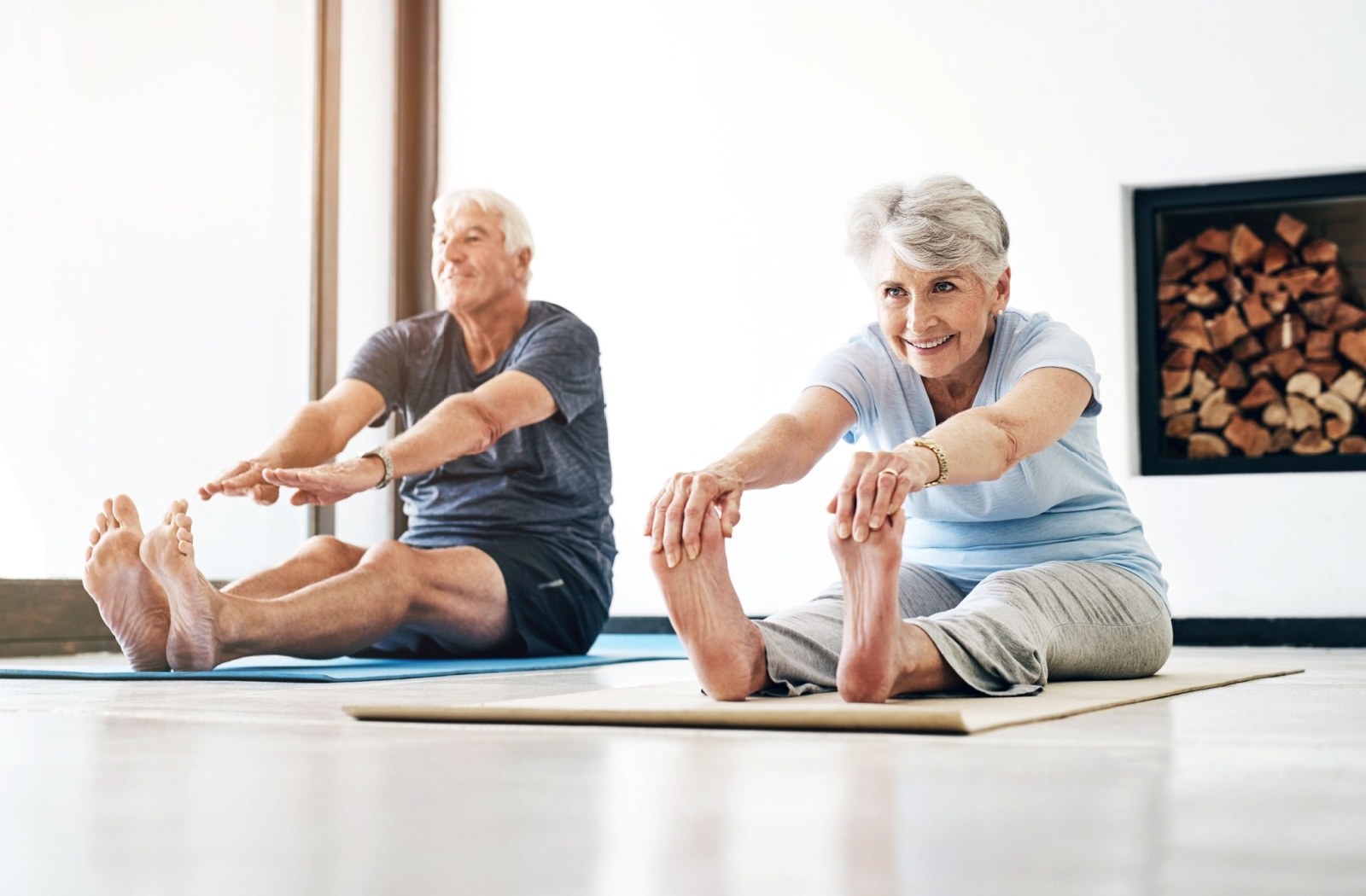 2 older adults sit on the floor and stretch to touch their toes to warm up before a Pilates class in senior living