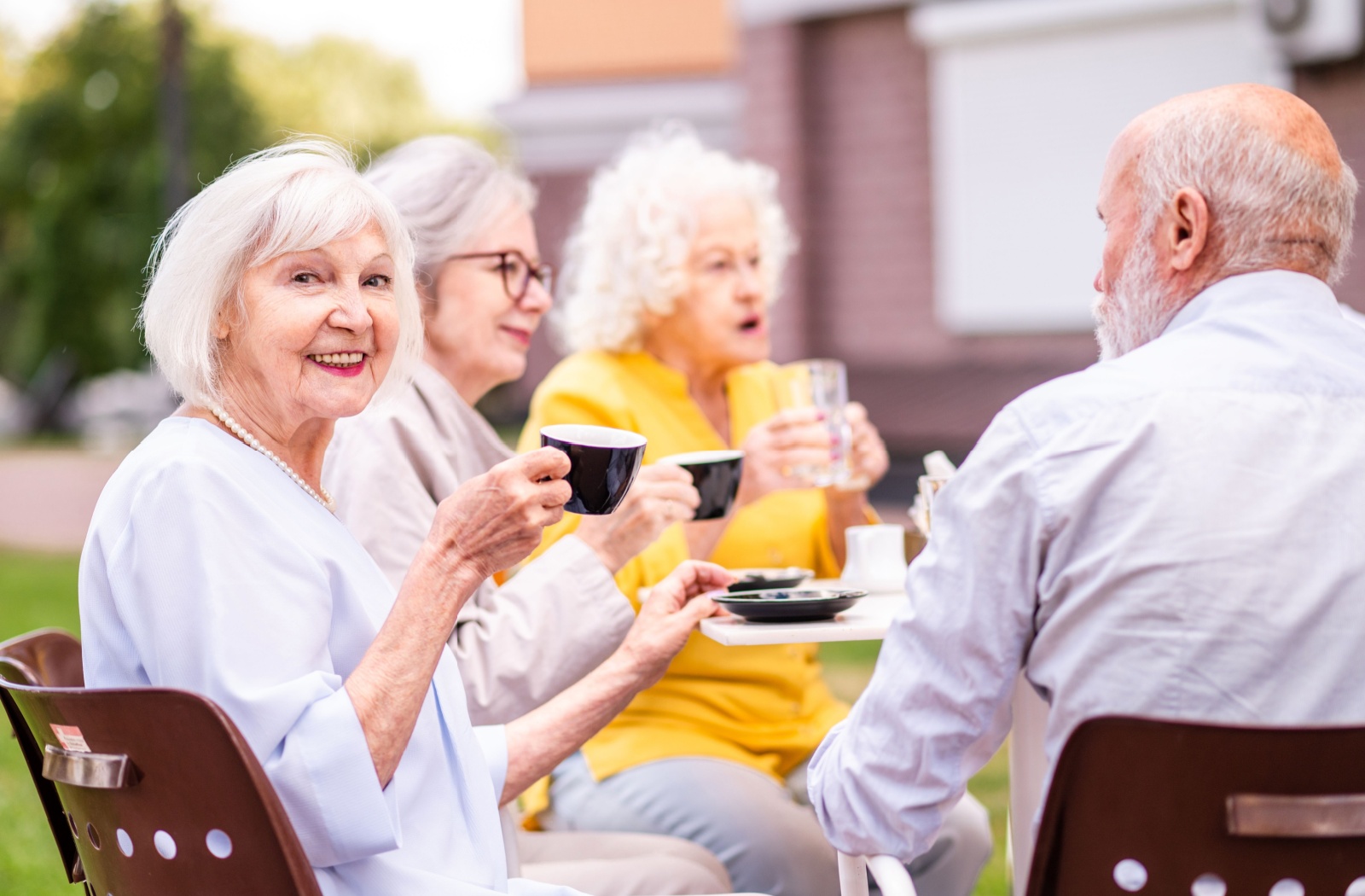 Seniors enjoy coffee and conversation outdoors smiling together in a social assisted living community setting
